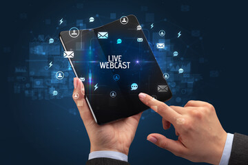 Businessman holding a foldable smartphone with LIVE WEBCAST inscription, social networking concept