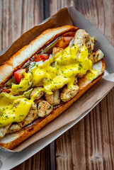 Philly cheese steak sandwich with meat, vegetables, cheese and sause in box on wooden table. street food