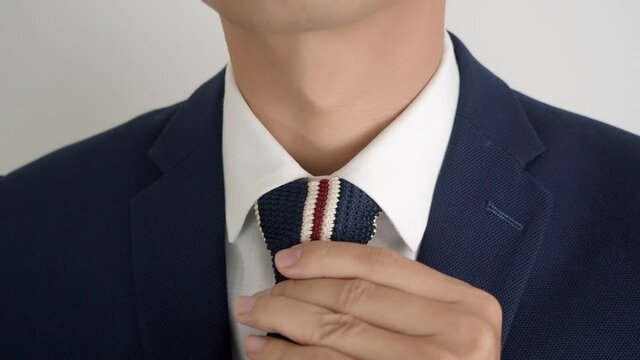 Asian business in formal dress adjusting fashionable knit neck tie then flutter to camera on white background.