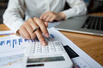 Close up of beautiful woman's hand using calculator keyboard. Laptop is standing by on the desk. Concept of accountant's work