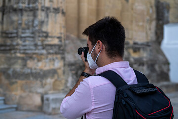 Hombre joven con mascarilla de viaje haciendo fotos al atardecer en un mirador del pueblo que visita