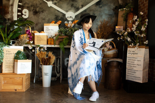 Traveler thai young women wear indigo tie dye paint shawl and scarf posing portrait sit read magazine book for take photo with decorate furniture at coffee shop on June 21, 2020 in Bangkok, Thailand
