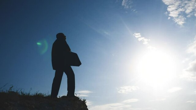 business success teamwork concept. man businessman in a jacket with a silhouette suitcase rises to the top of mountain looks into the distance, shows hand direction. lifestyle manager head set a goal