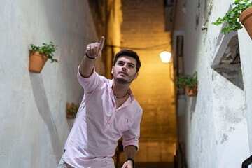 Hombre joven adolescente paseando por callejon iluminado  con flores por el pueblo 
