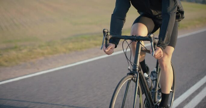 CU TRACKING Cyclist riding his bicycle on an empty rural road at dawn. 50 FPS Slow motion. Shot on RED Cinema camera