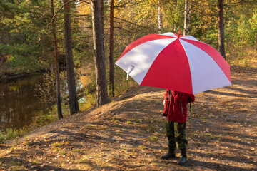 autumn story, a boy in a beautiful multi-colored forest with an umbrella on the shore of a natural reservoir