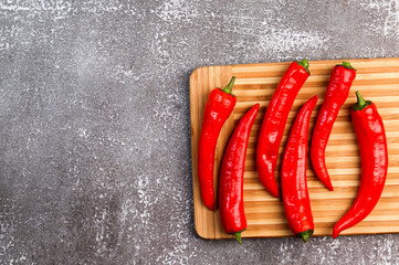 Red hot chili peppers on a rectangular cutting wooden board on a dark background. Top view, flat lay