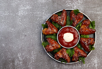 Baked chicken wings with sesame and sauce on a round plate on a dark background. Top view, flat lay