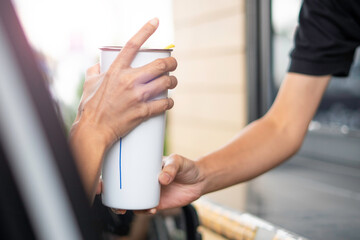 Hand in the car is picking up a personal cup of coffee from the salesman by driving through.