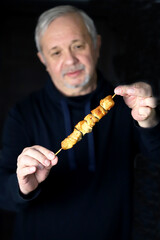 Selective focus. The man is eating a chicken skewer.