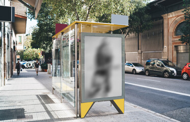 Picture of modern glass transparent bus stop with banner on side for advertising or promotional text message, urban setting with industrial transport station during summer sunny day