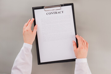 Female hands holding clipboard with business contract. Business woman reading document sitting at table in office. Business concept.