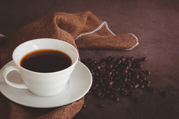 Refresh and energy drink concept. Hot black coffee or espresso in a white ceramic cup with brown cloth table and coffee beans on a dark stone table.