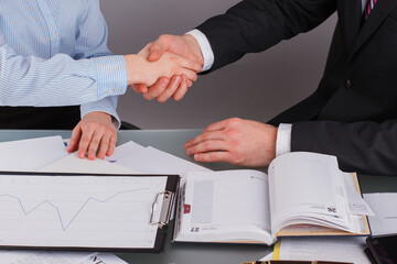 Partners shaking hands because signing contract or financial papers. Businessman shaking hands with his colleague or partner above desk in modern office. Success concept.