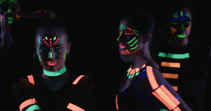 Studio, slow motion, close-up of a group of neon-painted dancers posing