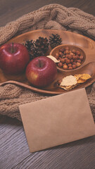 Autumn still life with apples and nuts. Autumn background with apples on a warm knitted scarf, a wooden plate, autumn leaves, hazelnuts and cones.