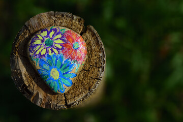 A brightly painted stone lies on a wooden post, against a green background, in nature