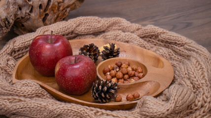 Autumn still life with apples and nuts. Autumn background with apples on a warm knitted scarf, a wooden plate, autumn leaves, hazelnuts and cones.
