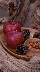 Obraz na płótnie Canvas Autumn still life with apples and nuts. Autumn background with apples on a warm knitted scarf, a wooden plate, autumn leaves, hazelnuts and cones.
