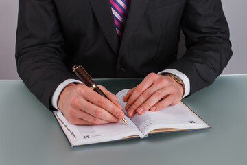 Businessman hand writing note on a notebook. Close up man in business suit writing in notebook sitting at table.