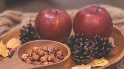 Autumn still life with apples and nuts. Autumn background with apples on a warm knitted scarf, a wooden plate, autumn leaves, hazelnuts and cones.
