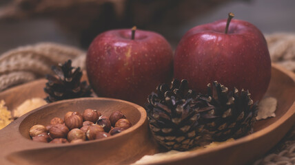 Autumn still life with apples and nuts. Autumn background with apples on a warm knitted scarf, a wooden plate, autumn leaves, hazelnuts and cones.