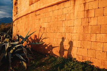 Silhouettes of a man and a woman on the orange wall of an ancient building on a sunny day.