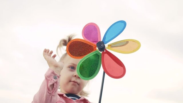 little daughter girl play pinwheel a wind toy. happy family concept lifestyle. child plays with windmill. portrait girl blonde kid holds flower toy spinning pinwheel. happy childhood