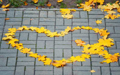 Сhildren folded autumn maple leaves in the shape of heart on the walkway. Autumn yellow leaves lie on the pavement in the shape of heart. Love in the fall.