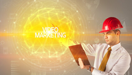 Handsome businessman with helmet drawing VIDEO MARKETING inscription, social construction concept