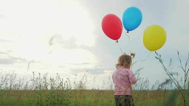 daughter little girl fun runs with balloons a on her birthday outdoors by field. dream happy family concept. child girl kid day lifestyle. child is running and balloons on a background of blue sky