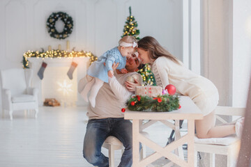 Family in a white room at the table. New year mood. On the background decorated fireplace and Christmas tree
