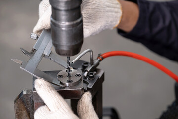 Technician wearing glove and measuring diameter of metal by using vernier caliper at the drilling...