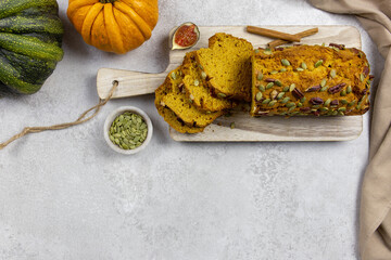 Pumpkin bread, cake on a wooden cutting board with pecans, pumpkin seeds and cinnamon spices. On a light background, with pumpkins and figs. Top view. Copy space.