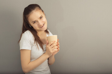 Invigorating coffee in a glass with you. Young woman drinks hot drink on gray background