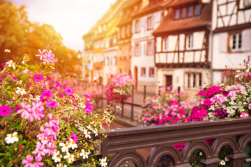 Fototapeta na wymiar Defocused background with scenic french old town architecture. View on blurred Colmar village with flowers by foreground, sunshine. Romantic place for travel destination. Alsace, France