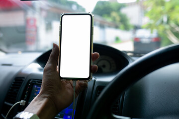 Mockup image of a hand holding and using white mobile phone with blank desktop screen while driving car on the road,The concept of a mobile screen has space to put text or advertisements.