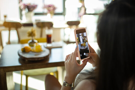 Point of view of a young woman taking a photo of her mango cake with her smartphone. Picture of food on screen.