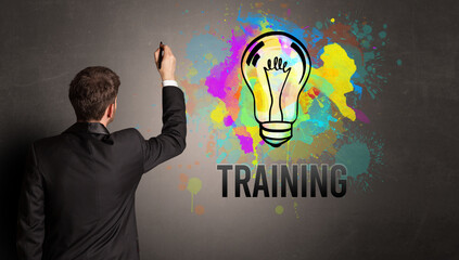 businessman drawing colorful light bulb with TRAINING inscription on textured concrete wall, new business idea concept