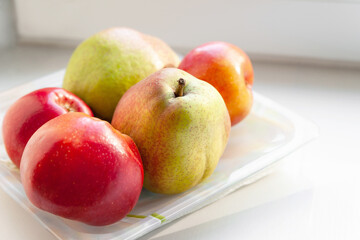 Autumn ripe fruits. Pears, apples and plums are stacked in a plate on a light background. Selective soft focus. Healthy organic food.