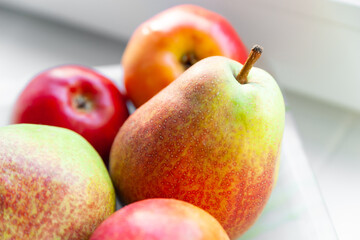 Close-up of autumn ripe fruits. Pears and apples are stacked in a plate on a light background. Selective soft focus. Healthy organic food.