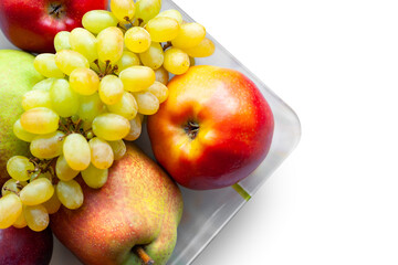 Top view of ripe fruits isolated on white background. Juicy pears, red apples and grapes are stacked in a plate. Selective soft focus. Healthy organic food.