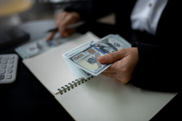 Closeup of business woman hands counting US dollar cash on the table.people holding Us dollar banknotes money ,using calculator calculate saving money with happy in office.