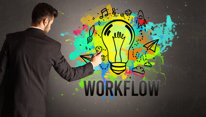 businessman drawing colorful light bulb with WORKFLOW inscription on textured concrete wall, new business idea concept