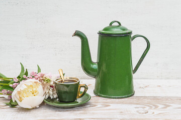 Coffee break in retro style. Green vintage cup of coffee and coffee pot, bouquet of peonies on white paint wooden background
