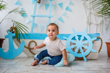 a little boy in a white t shirt and jeans sits and looks away against the background of a wooden boat