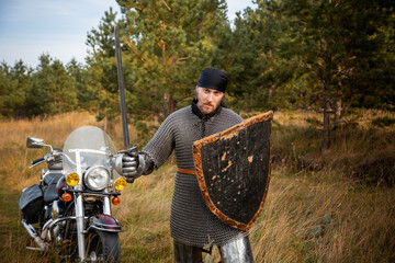 A medieval knight in chainmail with a shield and a sword in his hands stands against the backdrop...