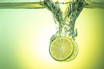 green lime slices falling under water with splashes on gradient background