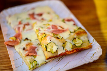 Eating of Italian pizza with mozzarella cheese, small courgettes zucchini, red tomatoes