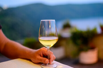 Hand with glass of cold dry white wine served outdoor in cafe at night in Italy